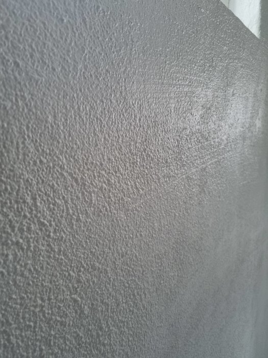 Närbild på en grå sprucken väggyta med ojämn textur