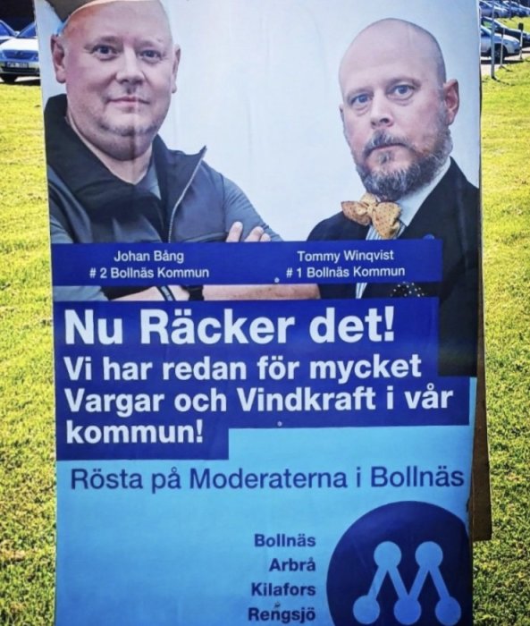 Politiskt reklamskylt med två män och text om vargar och vindkraft, uppmaning att rösta på Moderaterna i Bollnäs kommun.