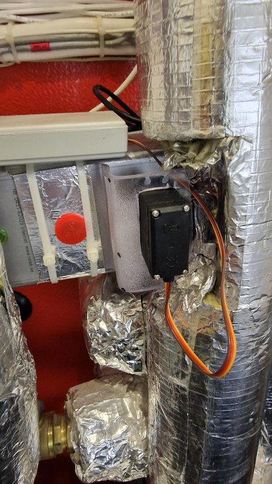 Elektrisk anslutningsbox monterad på isolerade ventilationsslangar med synliga kablar och rörkopplingar.