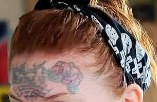 Person med bandana och en synlig tatuering på huvudet under upplyft hår.