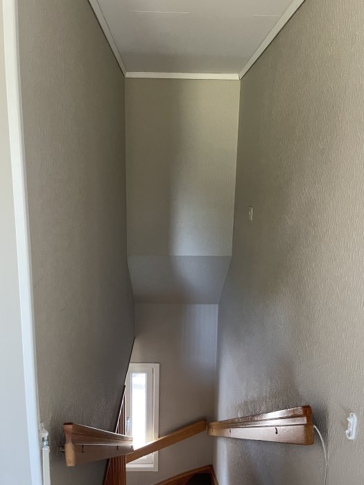 Trapphus med grått vävtapet och träledstång som visar behov av renovering.