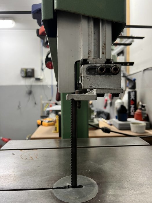 Bandsåg i verkstad med sågbladet i fokus, redo att såga genom en metallskiva vilande på arbetsbordet.