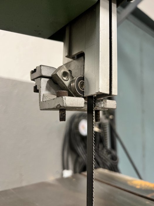 Närbild på en bandsågs bladguidning med justeringsskruvar och rullar fokuserad på mekanismens detaljer.