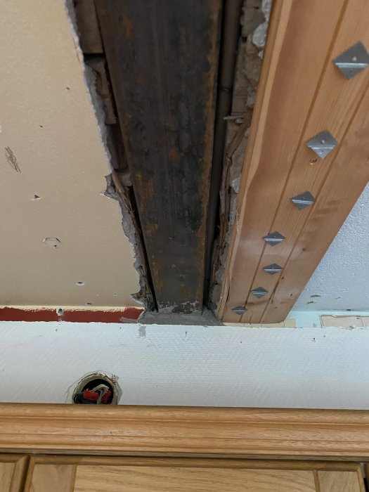 En bild som visar skador på en vägg och tak där gammalt trä och spikplåtar är synliga nära en eluttag.
