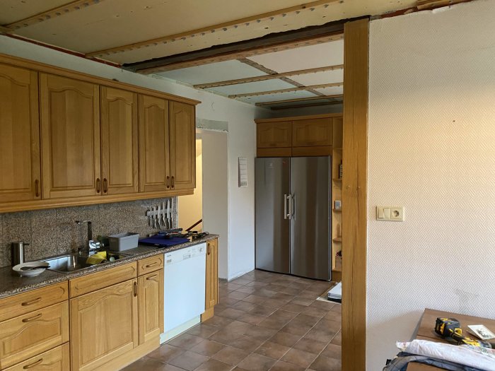 Kök under renovering med borttaget tak, träskåp och inbyggd kyl.