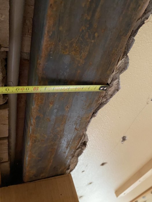 Måttband som mäter bredden på en synlig bjälke och VVS-rör i en öppen väggkonstruktion.