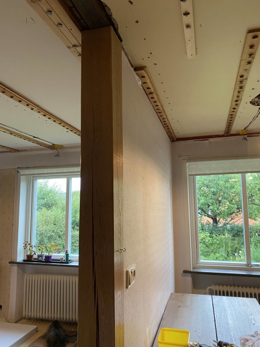 Delvis renoverat rum med isolerade väggar och synlig träpelare, med utsikt mot fönster.