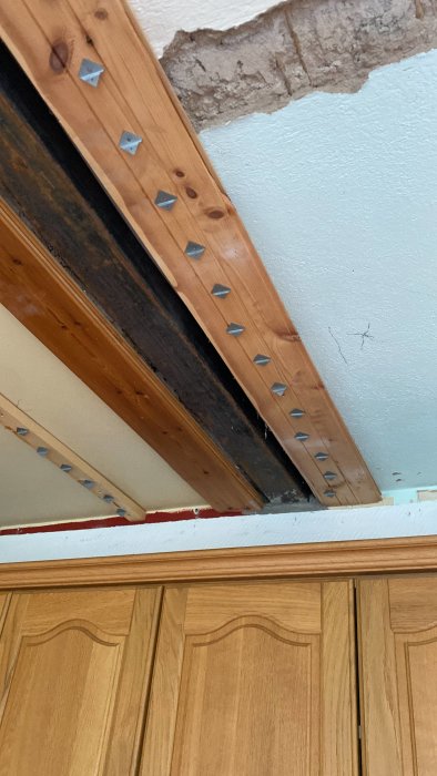 Skadad yta nära tak med synliga spikar och träbjälkar ovanför köksskåp.