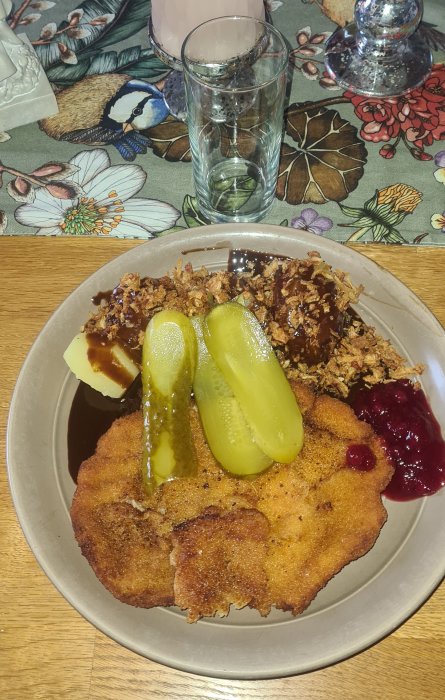 Hemlagad schnitzel med inlagd gurka, potatis, lök och röd sås på ett bordduk.