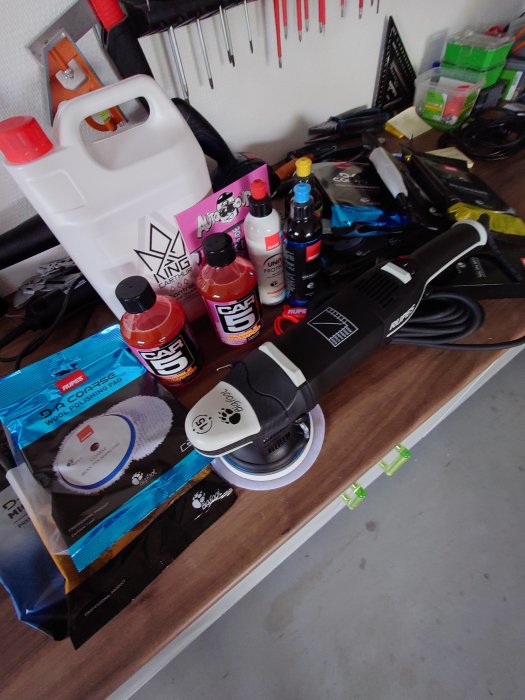 Poleringsmaskin och olika flaskor med bilvårdsprodukter på ett arbetsbord.