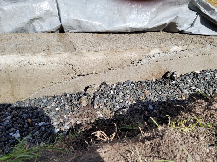 Gråsinglad grund till byggnad med plasttäcke och synliga sprickbildningar i betongen.