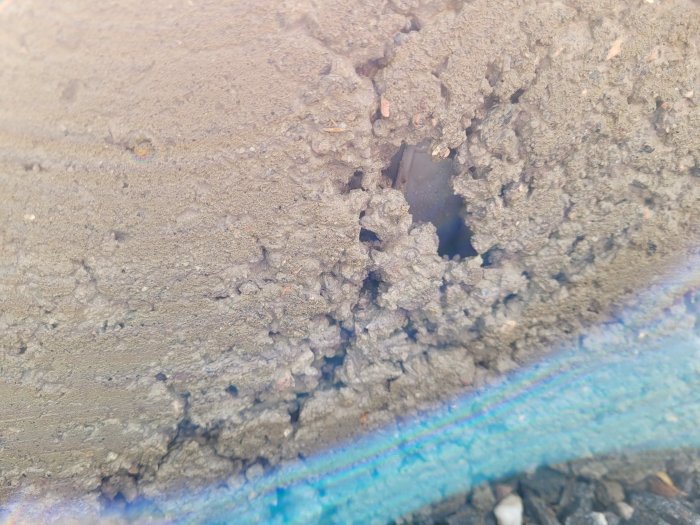 Närbild på fuktig betongyta med små håligheter och grov textur, solljus reflekterar en regnbågseffekt.