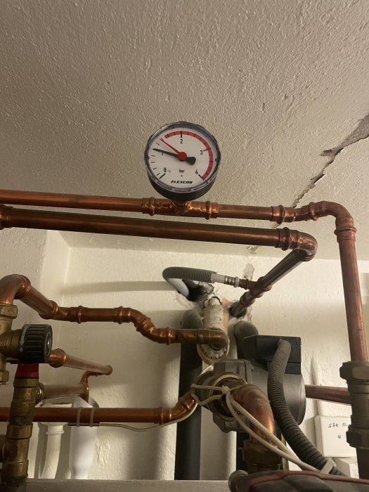 Manometer med röd visare på 1.5 bar monterad på kopparledningar och rörinstallationer.