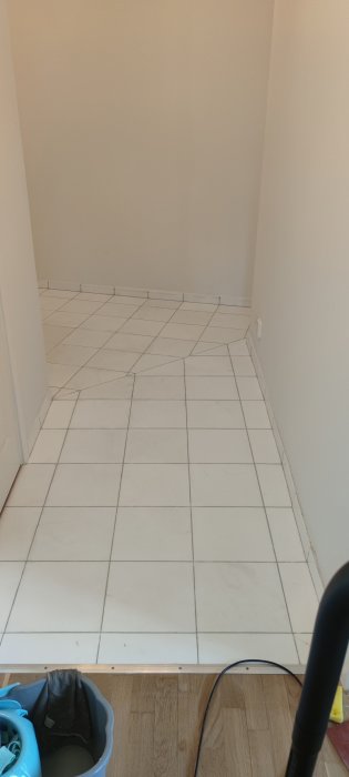 Nyinstallerade vita kakelplattor i ett rum med overgång till trägolv.
