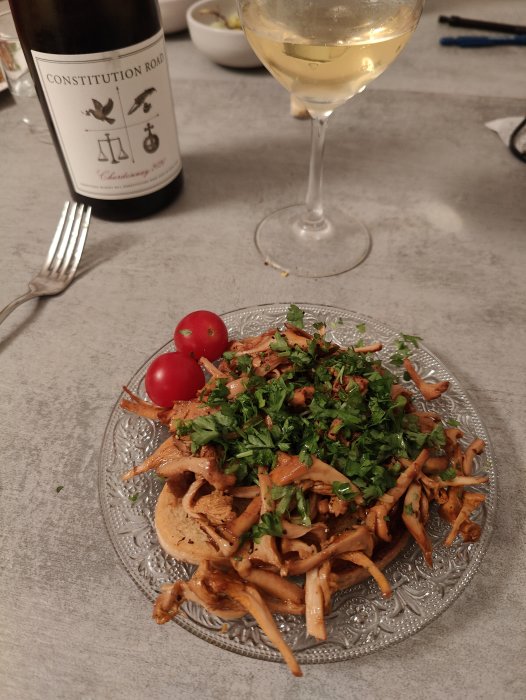 Open-faced sandwich with chanterelles and herbs on a plate, next to a glass of white wine and a wine bottle.