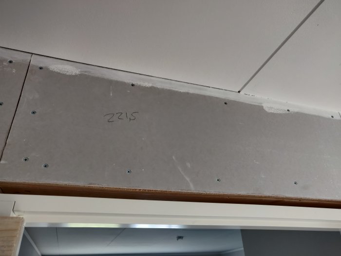 Gipsskiva fastskruvad i tak nära en trälist med påskrivet nummer 2215.