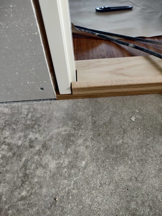 Detaljbild av golv och dörrfoder under montering med synligt trätrappsteg.