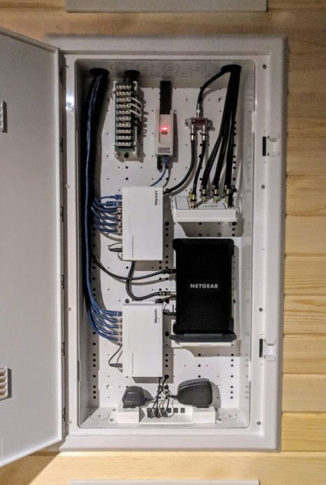 Öppet elskåp med organiserade elledningar, säkringsblock och en NETGEAR router, professionellt installerat på en vägg.