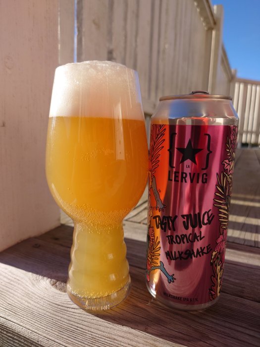 En milkshake IPA från Lervig i glas bredvid dess färgglada burk på ett träbord i solskenet.
