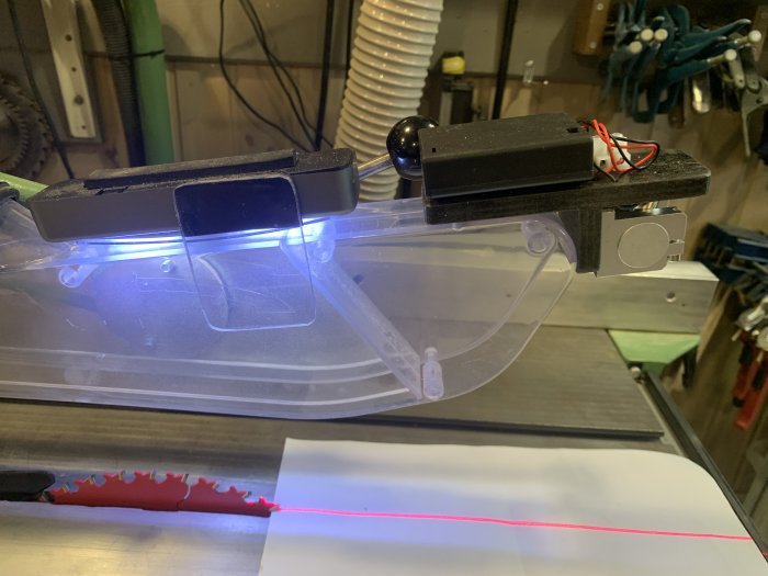 Laserlinje på sågbord markerar snittlinje, plasthuven modifierad för lasermontage, stabil laserposition och kablage.