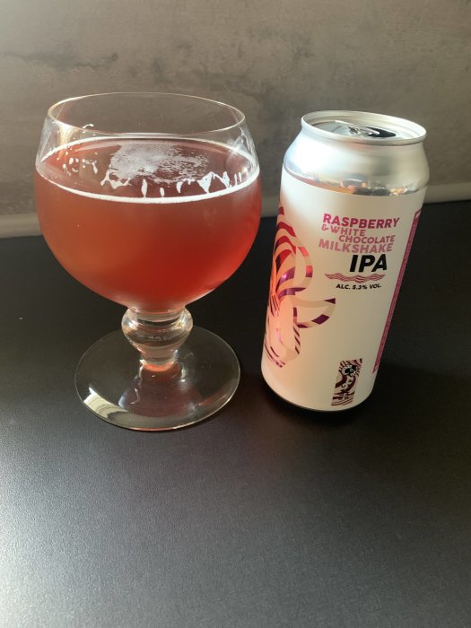 Ett glas med rosa öl bredvid en burk av Raspberry & White Chocolate Milkshake IPA.