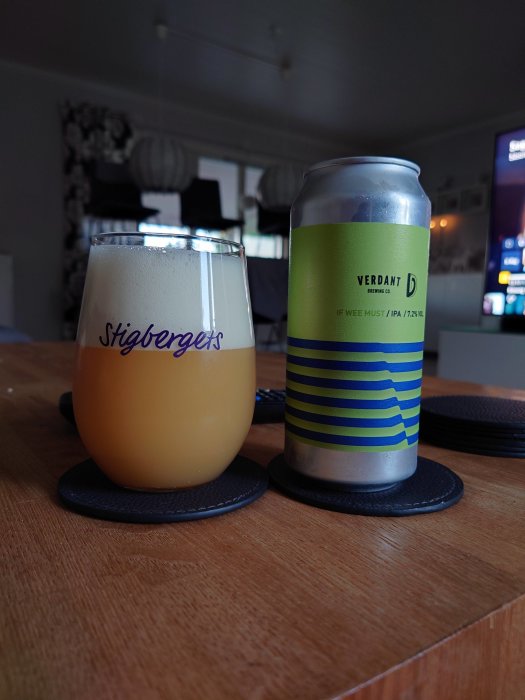 Ölglas med skummande öl bredvid en ölburk från Verdant på ett träbord.
