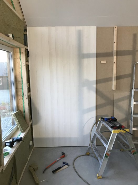 Nyinstallerad vit väggpanel i en stuga med verktyg och stege under arbete.