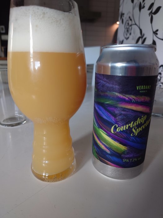 Ölglas med skumfylld öl bredvid en burk av Verdant Brewing Co's Courtship Spectrum IPA.