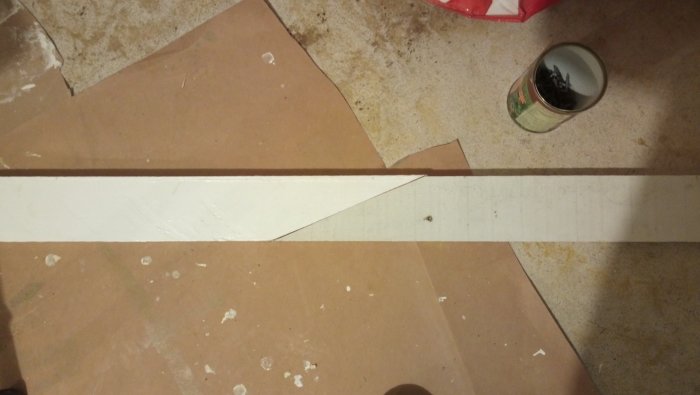 Två trälistbitar i vinkel ovanpå en smutsig yta, ej fastsatta, med en burk spik i bakgrunden.