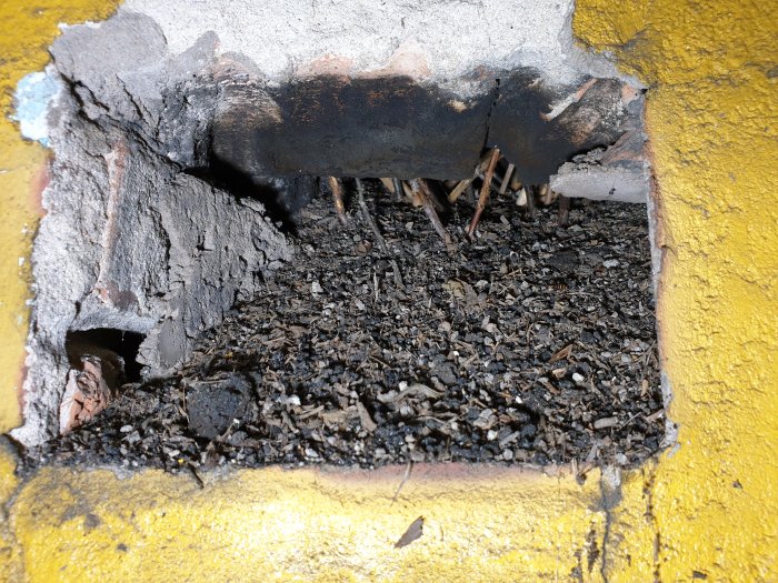 Närbild av ett murat och gulmålat fundament med en stor skada som avslöjar innanmätet och bråte.