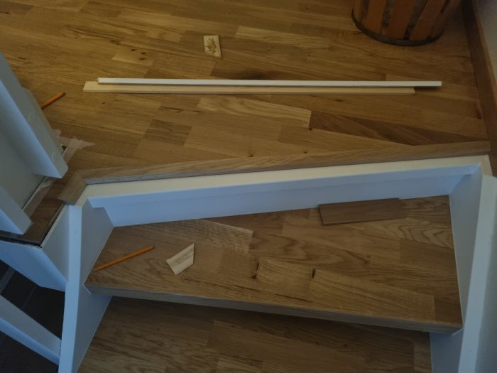 Vitmålade trappa-steg under konstruktion på ett trägolv med lösa träplankor och en penna.