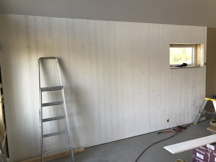 Invändigt hörn av ett rum under renovering med nyinstallerade vita panelväggar och en stege.