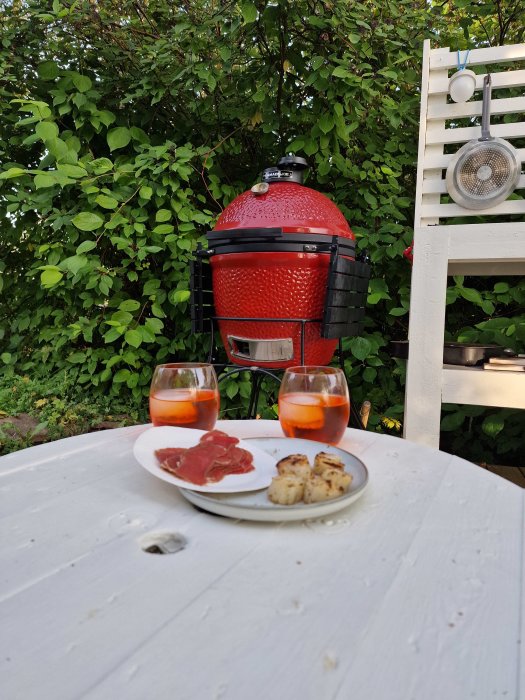 Keramikgrill och ett bord med en tallrik bresaola, pilgrimsmusslor och två glas Aperol Spritz.