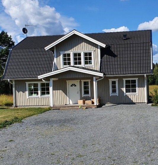 Tvåvåningshus med vit panel och svart tak under solig himmel.