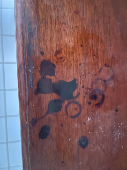 Vattenskador och mörka fläckar på en träyta, troligen tecken på mögel eller röta.