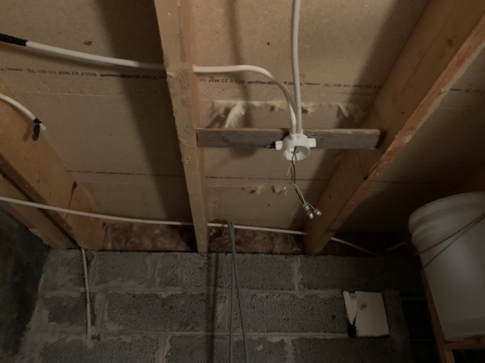 Oisolerad vind med exponerade träbjälkar, elinstallationer och rörledningar ovanför grå betongväggar.
