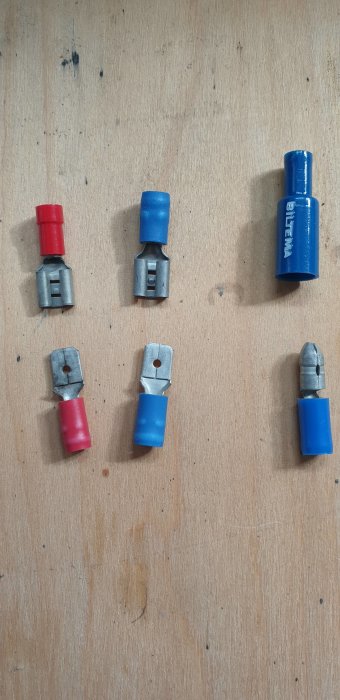 Elektriska flatstiftskontakter och runda kontakter i blått och rött sorterade på träbakgrund.
