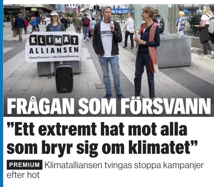 Två personer vid informationsstånd för Klimatalliansen på stads gata, med rubrik om klimatdebatt och hot.