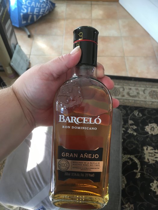 Hand håller en oöppnad flaska Barceló Gran Añejo rom som en hyllning.