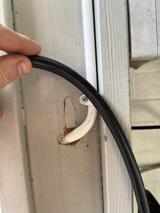 Tjock svart kabel lika tjock som laddkabeln, förs genom en vit kabelklamma på vägg.
