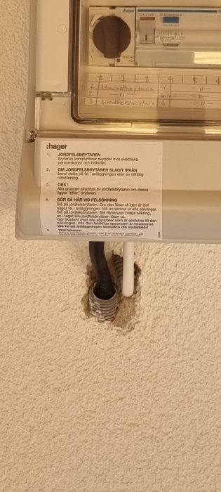 Elcentral med öppen kabelgenomföring och instruktionsetikett på väggen.