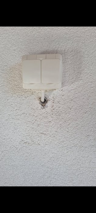 Väggmonterad ljusströmbrytare på strukturtapet med synlig elkabel.