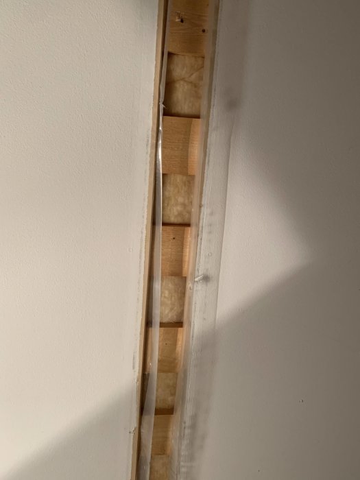 En väggöppning visar isoleringsmaterial mellan träreglar i en väggkonstruktion.