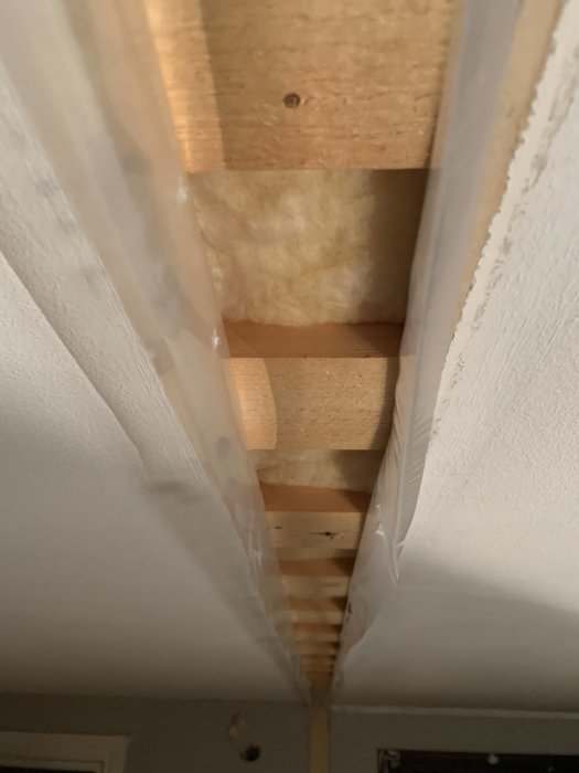 Vy uppåt mellan oupptäckta takbjälkar och isoleringsmaterial i ett pågående byggprojekt.