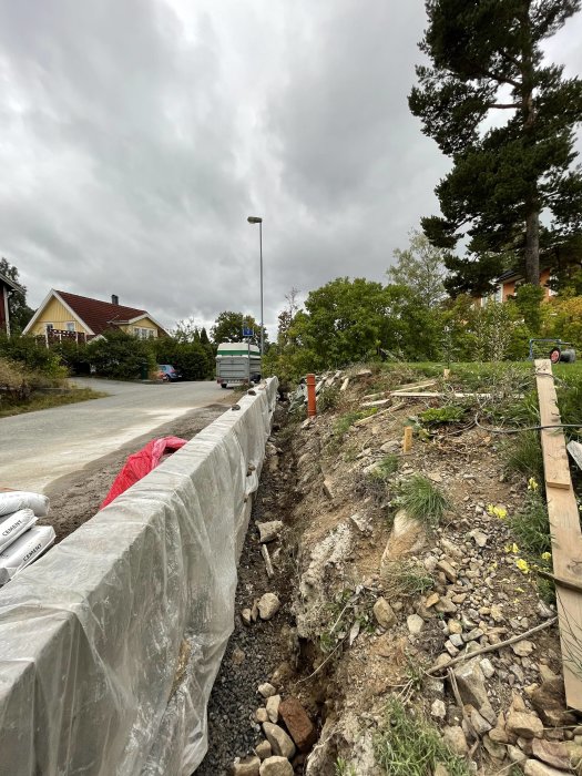 Utgrävd grund med skalblock och stenkistor för dränering vid byggprojekt, täckt av plastfolie.