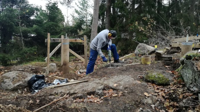 Person som arbetar med att borra i sluttande berg för plintfundament vid byggprojekt.