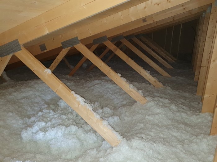 Nyisolerat vindutrymme med träbjälkar och mineralullsisolering.