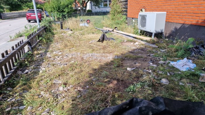 Trädgård med spillror och skräp efter byggarbete, inkluderande betongpannor och bråte på gräsmattan.