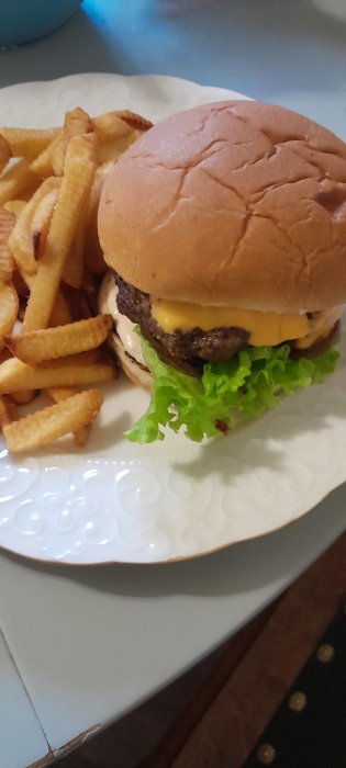 Hamburgare med högrev och smält ost i bröd med sallad, serverad med krulliga pommes frites.