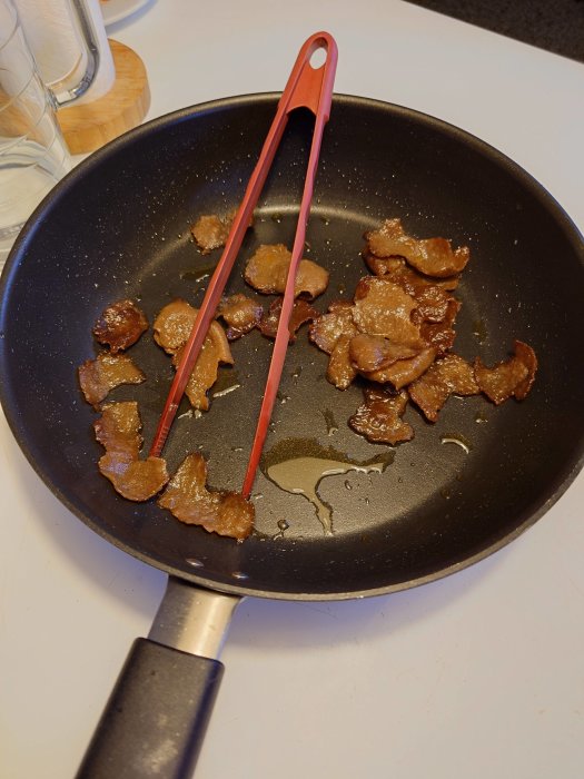 Stekpanna med stekt kebabkött och röda tång på ett köksbord.